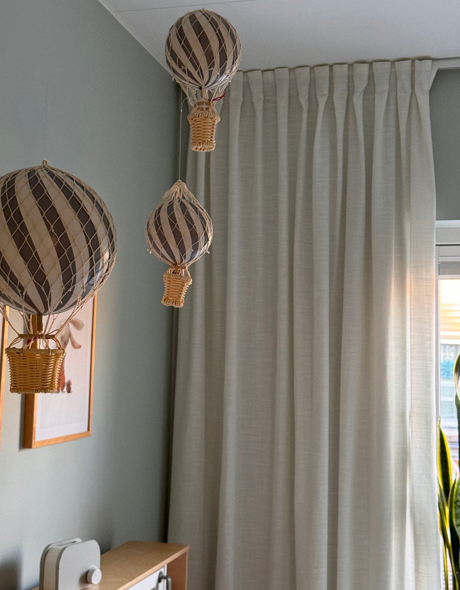 Vit gardin med motveck uppsatt i barnrum med luftballonger framför